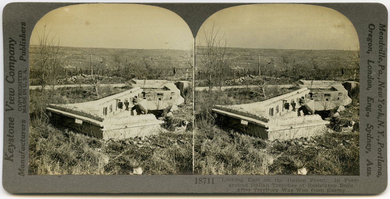 Horizontale, sepia stereokaart met een man in uniform die achter een reeks betonnen loopgraven in een open veld staat. Keystone Stereograph nummer 18711. De titel luidt door Keystone View Company