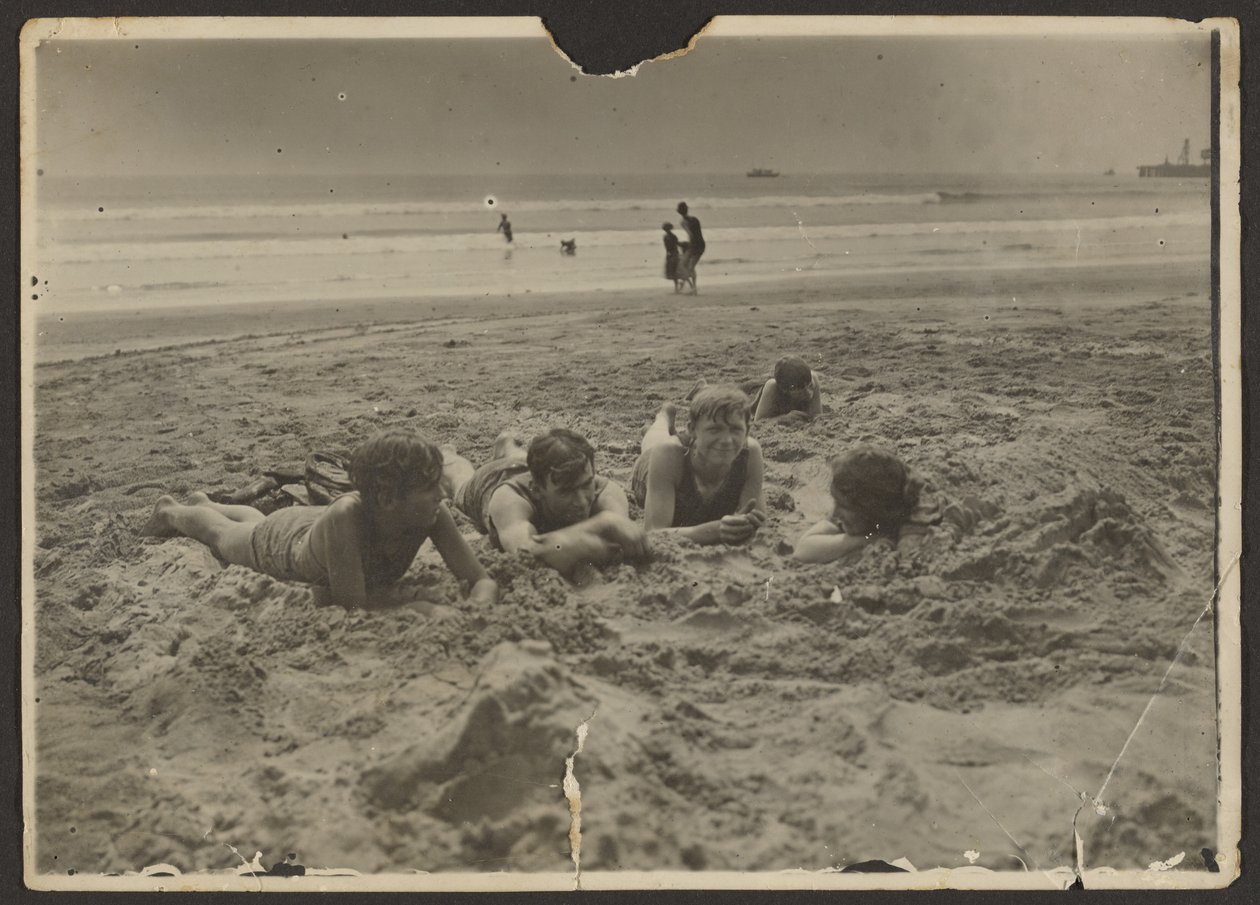 [Kinderen liggen in het zand op het strand]. door Louis Fleckenstein