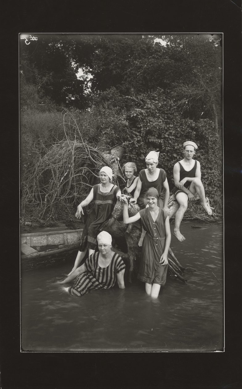 Groep van één man en vier vrouwen in badpakken zittend aan een rivierbank door Oscar C. Kuehn