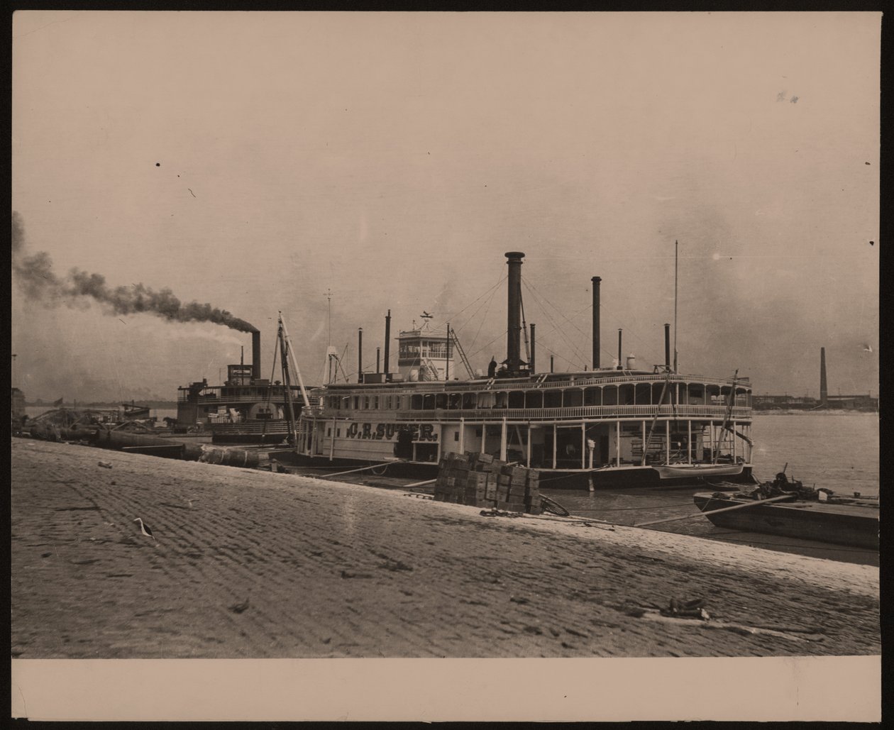 Horizontale, zwart-wit foto van de stoomboot C.R. Suter. Een andere stoomboot ligt erachter en kratten zijn op de oever gestapeld door William G. Swekosky